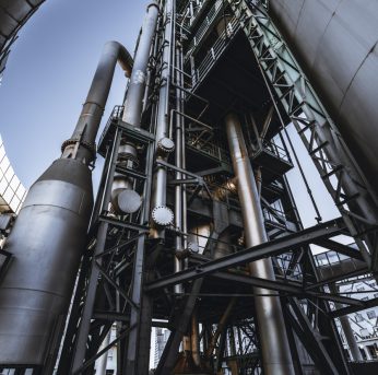 An industrial fuel factory building A wide-angle vertical view from the bottom of a modern oil refinery or a contemporary fuel factory facility in an industrial zone, with a round bridge, plenty of pipes, metal beams, tanks, and stairs